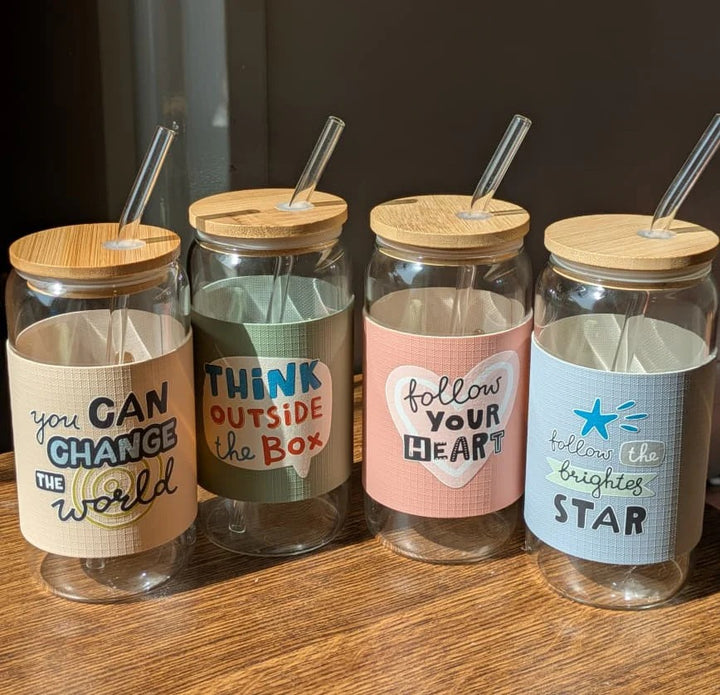 Four glass jars with motivational labels and wooden lids on a wooden surface.