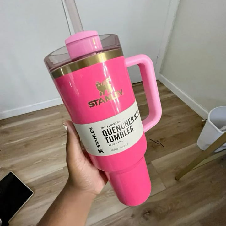 Pink tumbler with handle held by a hand on a wooden floor.