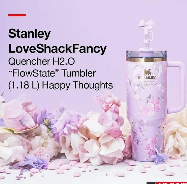 A pink Stanley LoveShackFancy Quencher H2.O tumbler with a floral pattern, accompanied by a reusable straw, displayed alongside pink and white flowers.