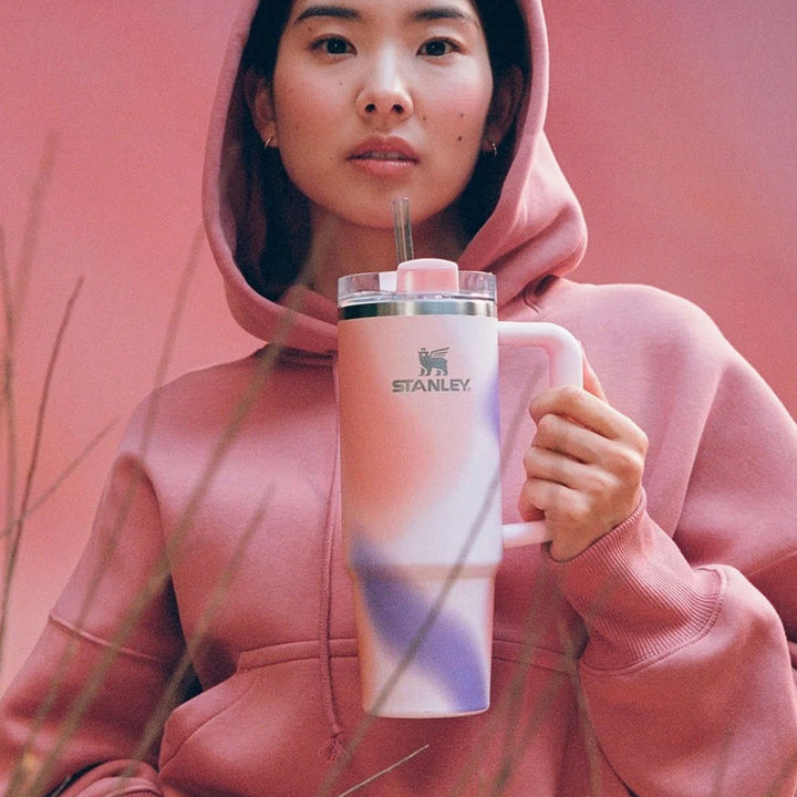 Person wearing a pink hoodie holding a pink Stanley tumbler with a straw against a pink background