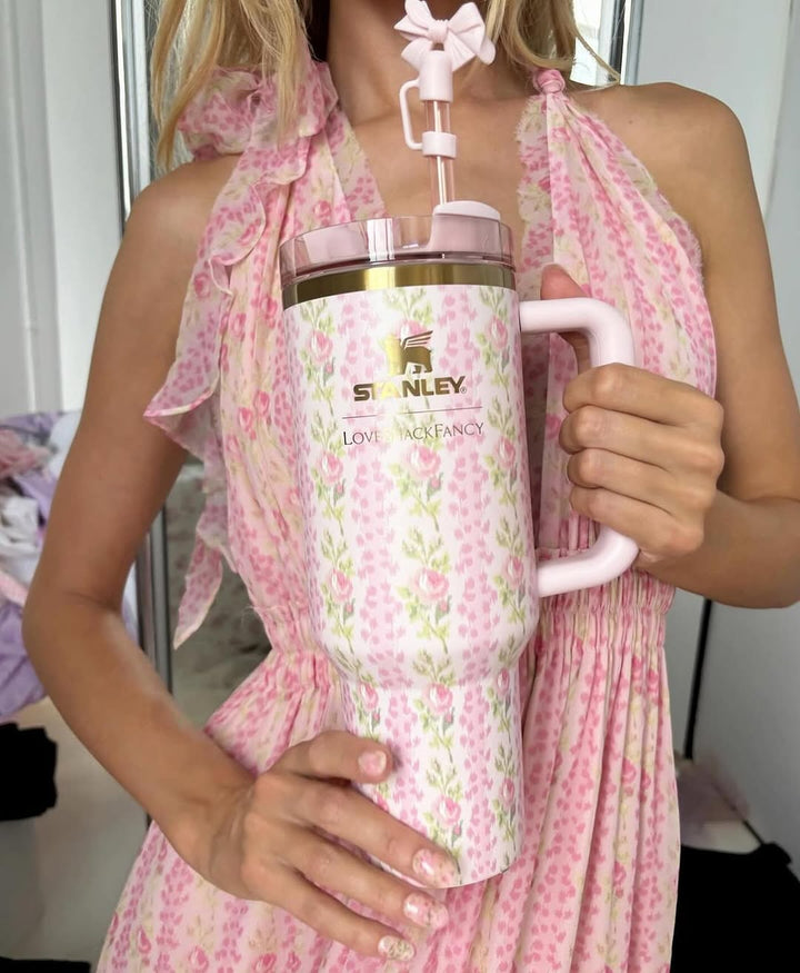 A person holding a pink tumbler with a 'Stanley' logo and 'LoveShackFancy' branding, featuring an oversized bow design.