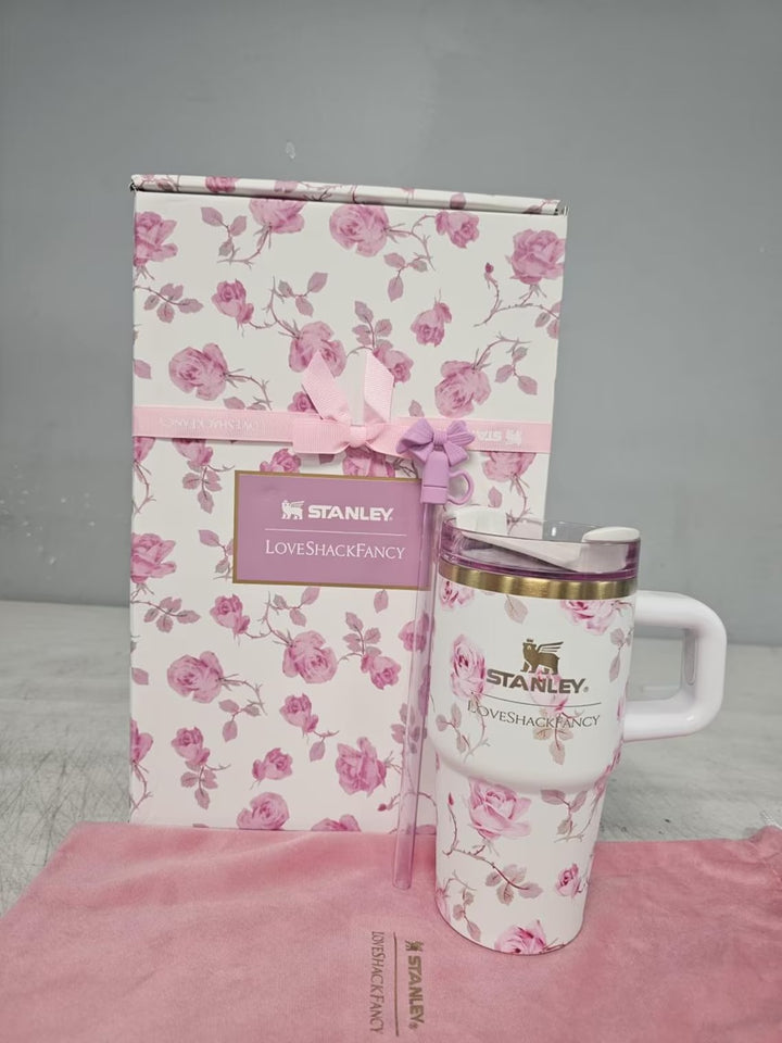 Stanley mug and floral-patterned box on a pink surface with a gray background