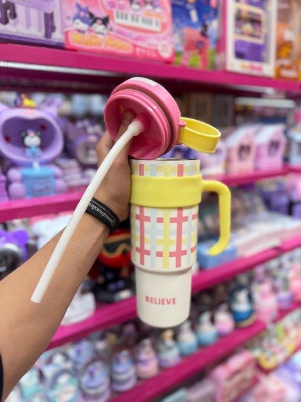 Colorful tumbler with a straw held in front of a store shelf with toys.